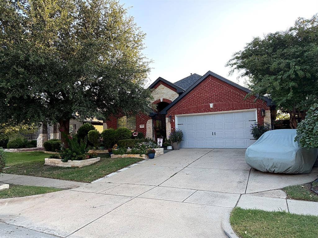 416 Wooded Creek Avenue, Wylie, TX 75098 Traditional exterior featuring red brick and stone masonry, multi-gabled roofline, concrete driveway, and established landscape with mature trees and stone-bordered garden beds