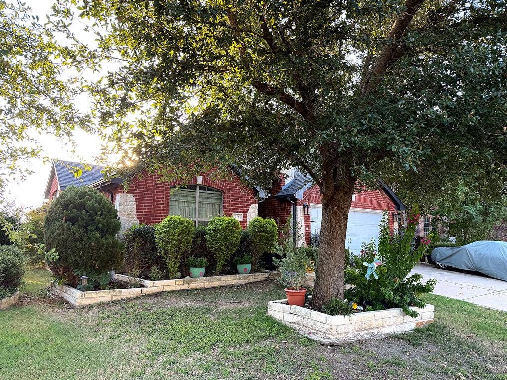 416 Wooded Creek Avenue, Wylie, TX 75098 Red brick exterior featuring limestone masonry accents, arched window detailing, a multi-car garage, and tiered stone garden beds
