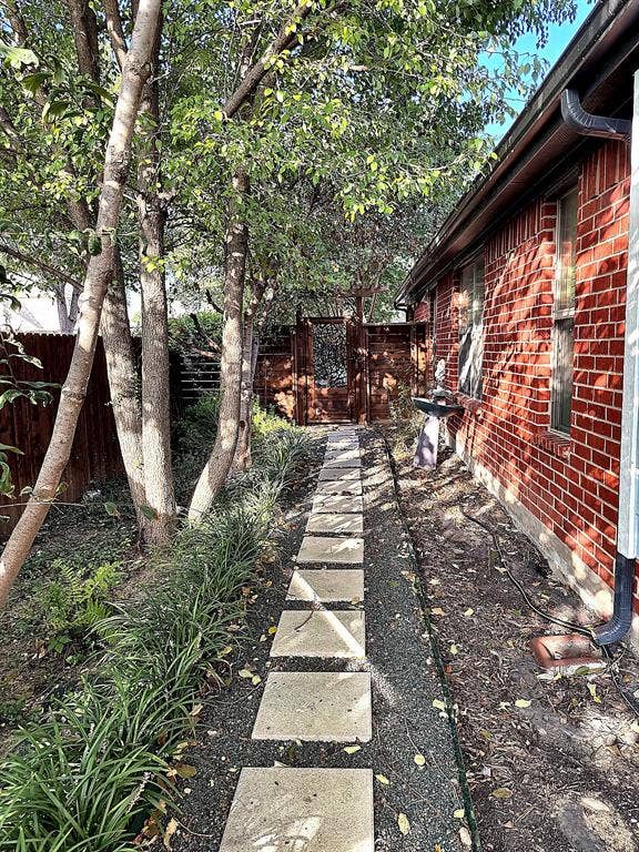 416 Wooded Creek Avenue, Wylie, TX 75098 Exterior pathway featuring a red brick facade, square stone pavers, gravel landscaping, and a decorative wooden gate