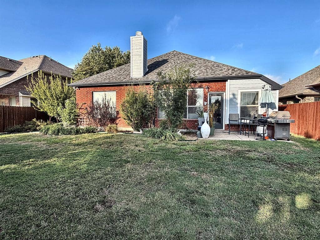 416 Wooded Creek Avenue, Wylie, TX 75098 Rear exterior featuring a brick and siding facade, a paved patio, a centered chimney stack, and a fenced backyard