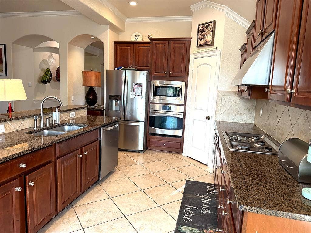 416 Wooded Creek Avenue, Wylie, TX 75098 Kitchen featuring dark wood cabinetry, stone countertops, stainless steel appliances, a built-in wall oven and microwave, and tile flooring
