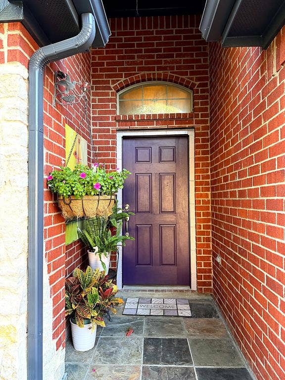 416 Wooded Creek Avenue, Wylie, TX 75098 Red brick exterior entryway featuring a six-panel door, arched transom window, and multi-tone stone tile flooring