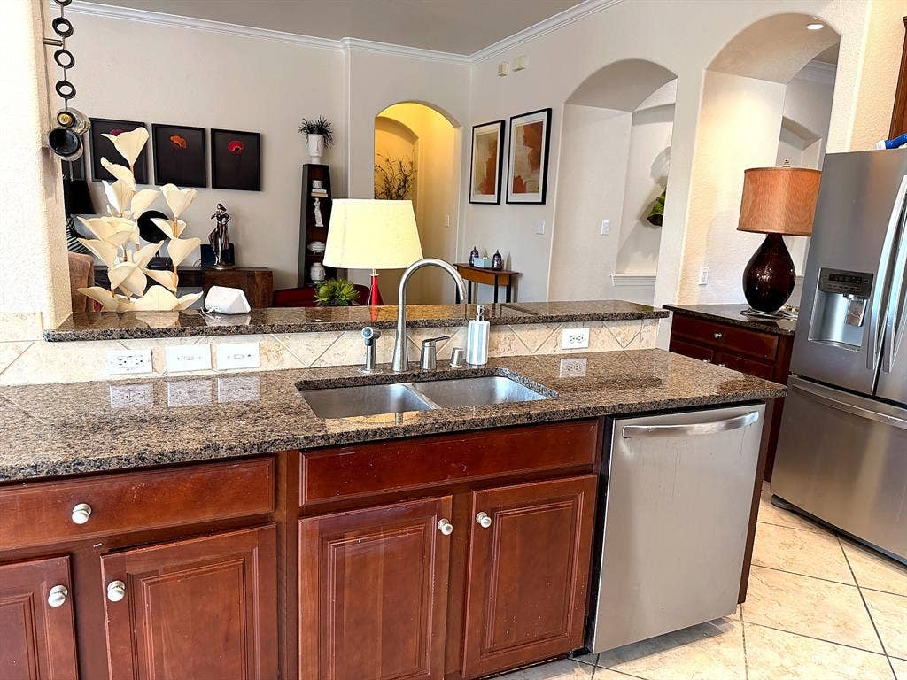 416 Wooded Creek Avenue, Wylie, TX 75098 Kitchen featuring dark wood-finish cabinetry, stone countertops, stainless steel appliances, a dual-basin sink, and decorative arched wall niches