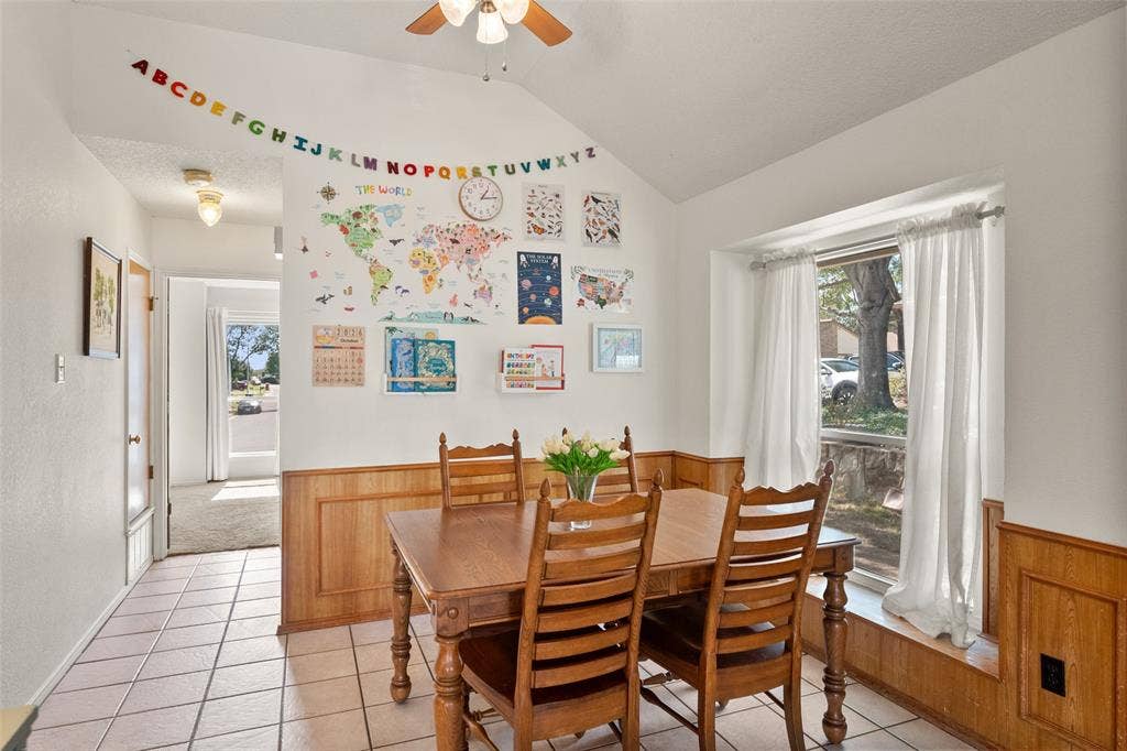 Dining area featuring a vaulted ceiling, wood wainscoting, ceramic tile flooring, and a large window bay