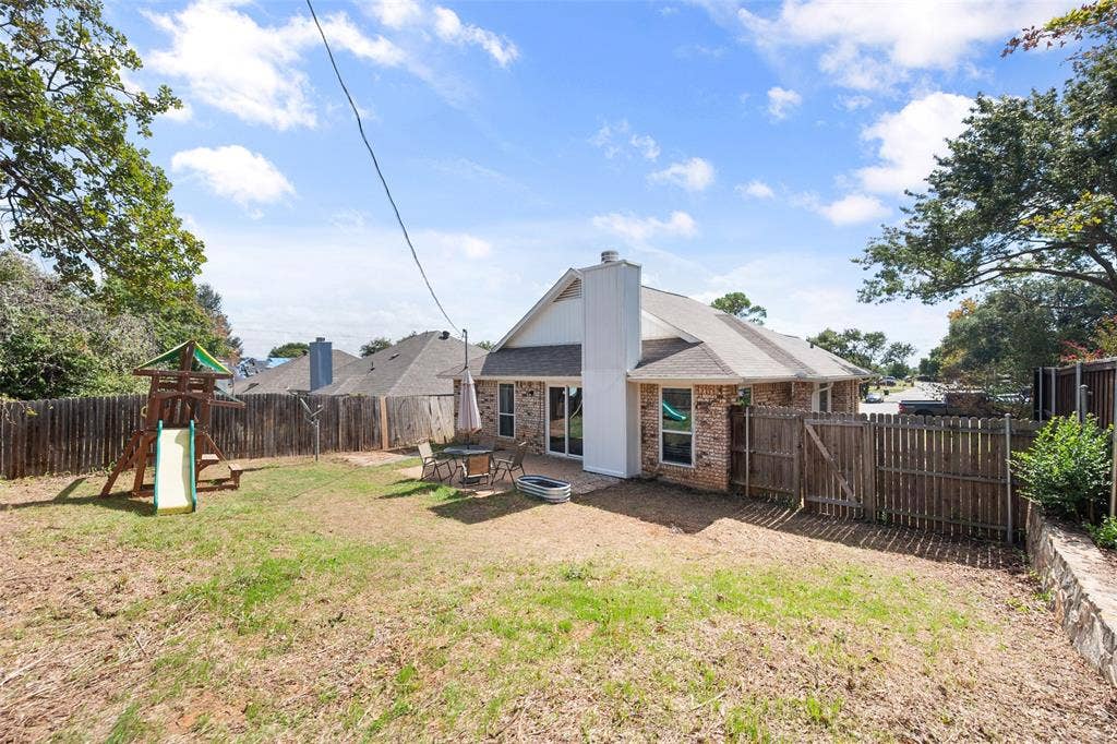 Rear exterior featuring a brick and white siding facade, a paved patio, and a fenced backyard
