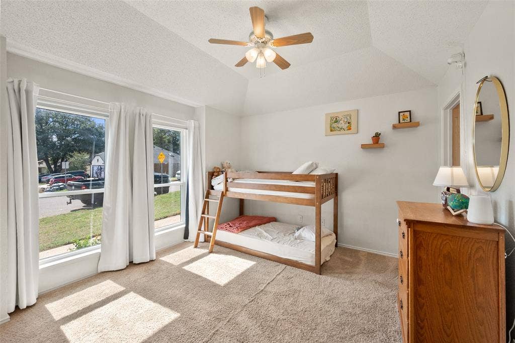 Vaulted ceiling, neutral wall-to-wall carpeting, multiple windows with natural light, and a central ceiling fan with integrated lighting