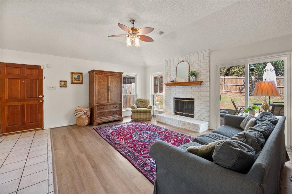 Living area featuring vaulted ceilings, wood-finish flooring, a white brick fireplace with a wood mantel, and sliding glass doors