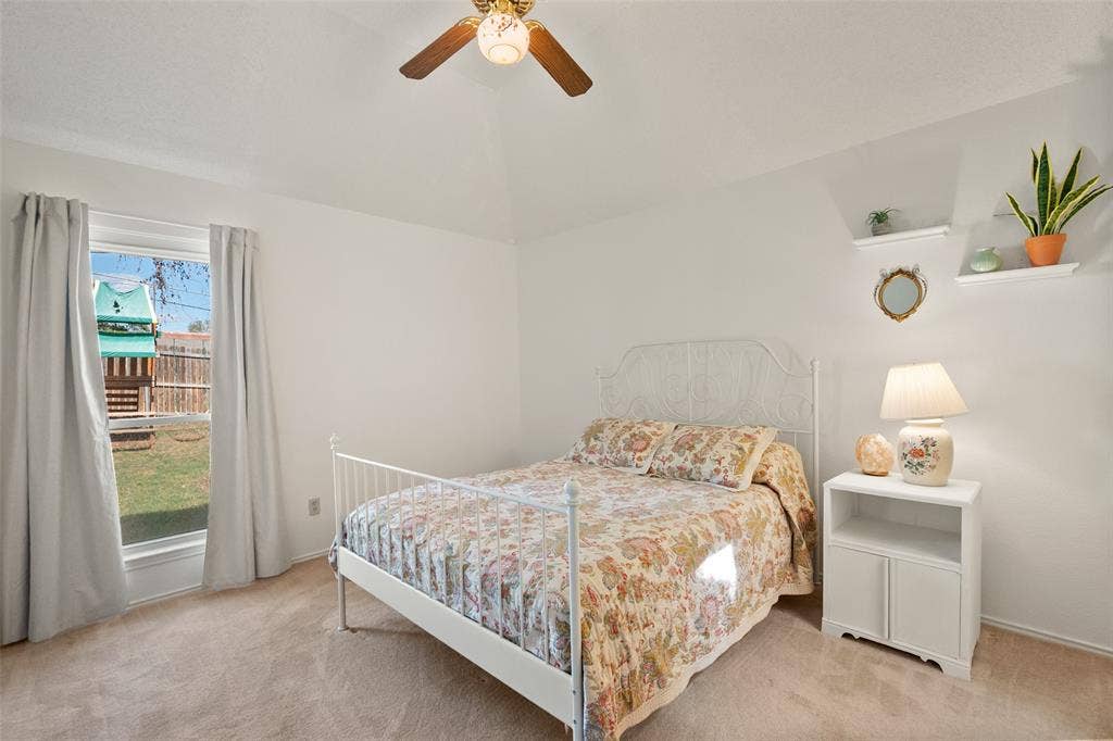 Vaulted ceiling featuring a central ceiling fan, carpeted flooring, and wall-mounted shelving