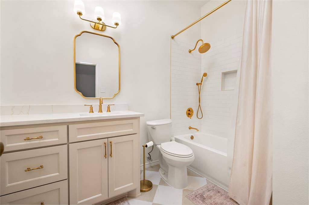 Bathroom featuring a vanity with white stone countertop, gold-toned hardware and fixtures, a custom-shaped mirror, and a tiled tub-shower combination with a built-in recessed niche