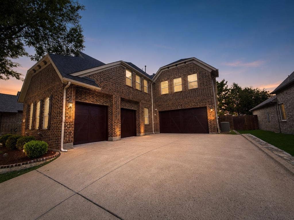 13812 Nash Lane, Frisco, TX 75035 Brick exterior with multiple gabled rooflines, featuring dark wood garage doors and complementary exterior lighting