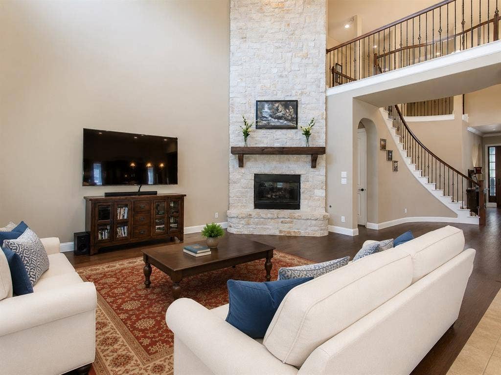 13812 Nash Lane, Frisco, TX 75035 Two-story living area featuring a stone-clad fireplace with a wood mantle, rich wood-finish flooring, and a curved staircase with wrought iron balusters