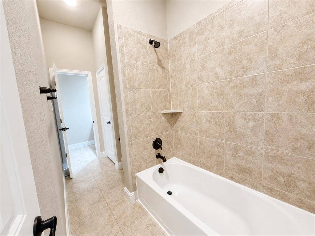 13812 Nash Lane, Frisco, TX 75035 Bathtub and shower combination featuring neutral-toned tile surround, matte black fixtures, and an integrated corner shelf
