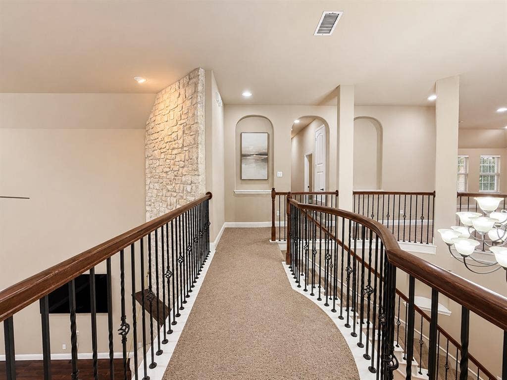 13812 Nash Lane, Frisco, TX 75035 Second-story hallway featuring a curved wrought iron and wood-finish railing, plush neutral carpeting, stone accent wall, and recessed lighting