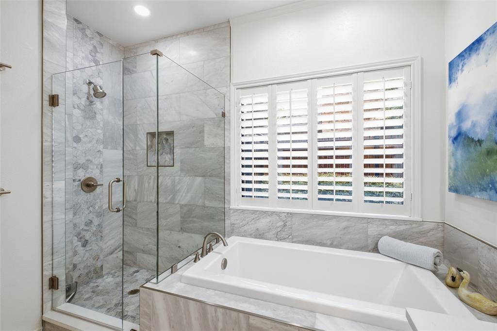 4115 Brooktree Lane, Dallas, TX 75287 Frameless glass shower with marble-look tile and pebble accents beside a deep soaking tub—your nightly reset.