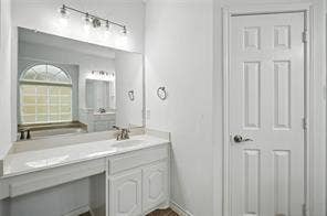 Bathroom featuring a vanity with an integrated sink, expansive wall-mounted mirror, four-light vanity fixture, and six-panel interior door