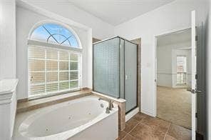 Oversized arched window, jetted soaking tub with tile surround, glass-enclosed shower, and tile flooring