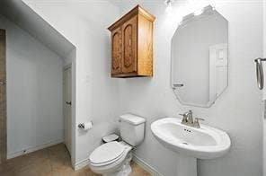 Bathroom featuring a wall-mounted wooden cabinet, an oval pedestal sink with a dual-handle faucet, a wall-mounted octagonal mirror, and tile flooring