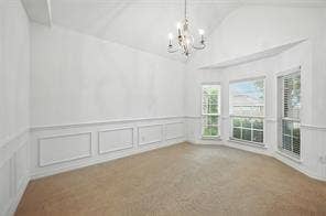 Vaulted ceiling with a multi-arm chandelier, bay window, and wall wainscoting