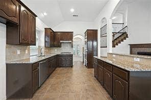 Kitchen featuring dark-finish cabinetry, stone-style countertops, tile flooring, high vaulted ceilings, and a staircase with iron balusters