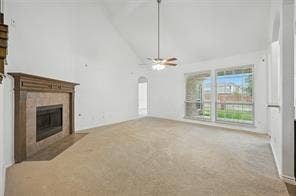 Vaulted ceilings, expansive windows, carpeted flooring, and a fireplace with a wood mantle and tile surround, illuminated by a ceiling fan