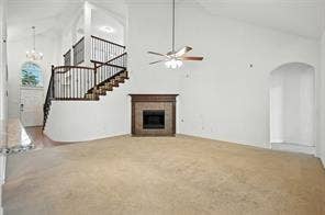 High-ceiling interior featuring a fireplace with stone surround, curved staircase with iron balusters, arched wall niche, and ceiling fan