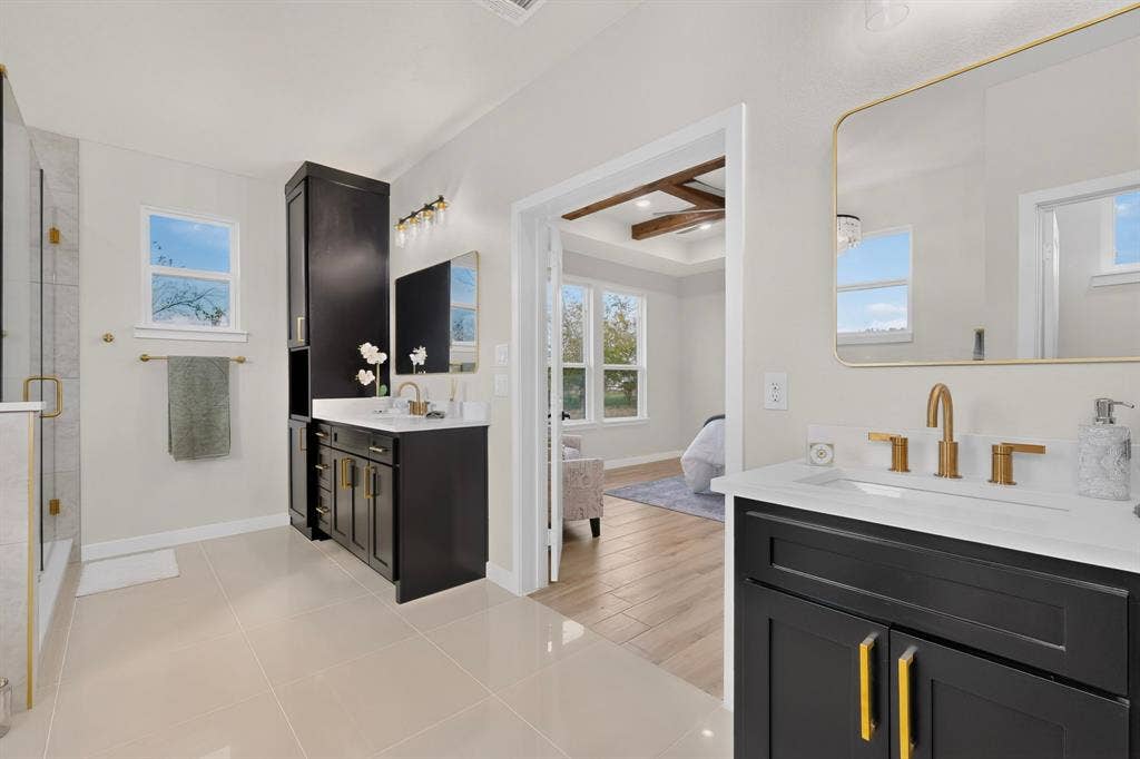102 Nicklaus Drive, Sulphur Springs, TX 75482 Dual dark-finish cabinetry vanities with white countertops, integrated sinks, gold-tone hardware, and matching wall-mounted mirrors