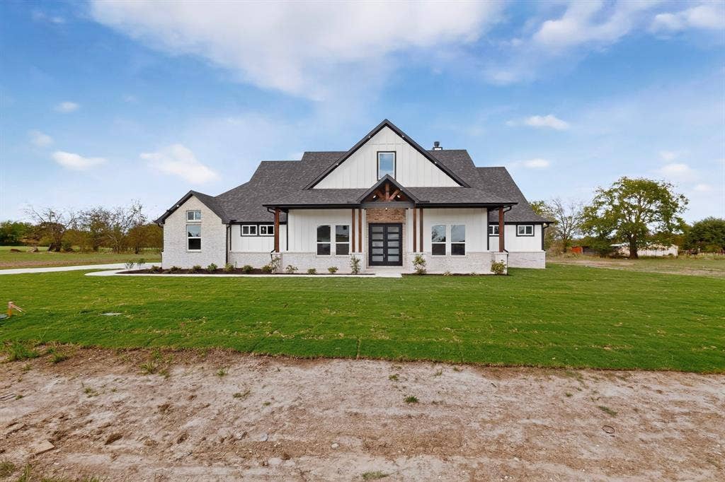 102 Nicklaus Drive, Sulphur Springs, TX 75482 Modern farmhouse exterior featuring vertical siding, stone masonry accents, a pitched roofline, timber beam detailing, and double-entry doors