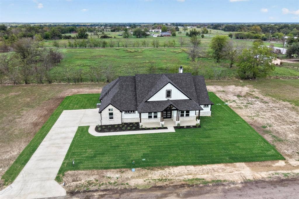 102 Nicklaus Drive, Sulphur Springs, TX 75482 Modern farmhouse exterior featuring a stone and siding facade, steep-pitched roof, covered front entryway, and an expansive manicured lawn with a concrete driveway