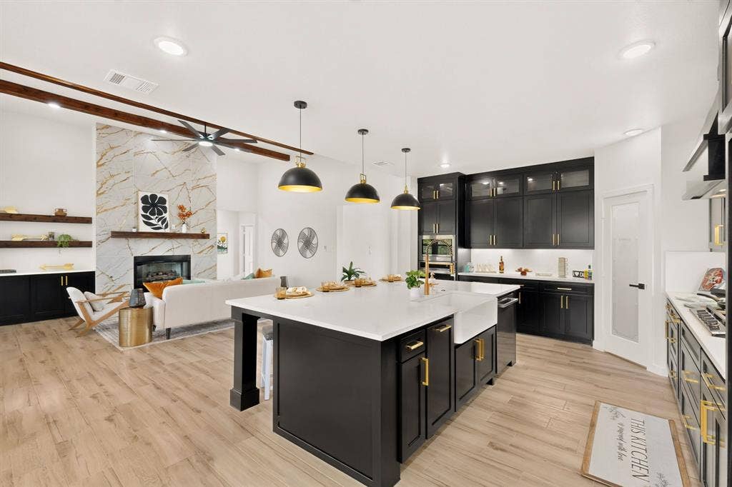 102 Nicklaus Drive, Sulphur Springs, TX 75482 Kitchen featuring a large central island with quartz countertops, custom dark cabinetry, wood-finish flooring, three pendant lights, and a stone-surround fireplace with wood ceiling beams