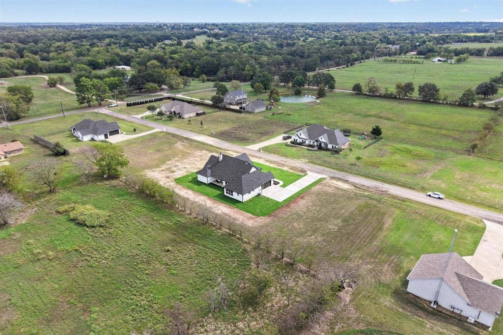 102 Nicklaus Drive, Sulphur Springs, TX 75482 Aerial perspective featuring a multi-gabled architectural design, dark shingle roof, integrated garage, and expansive grounds situated within a rural setting
