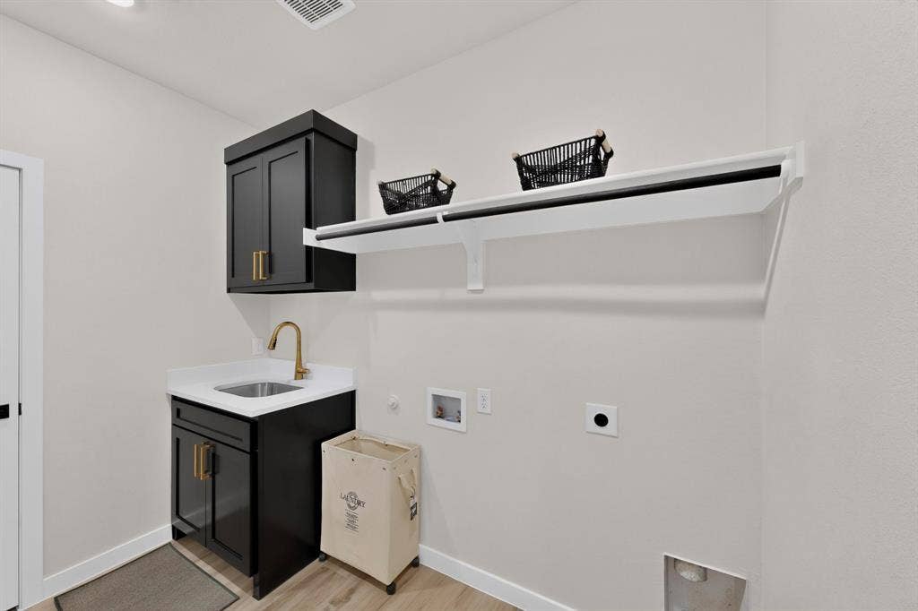 102 Nicklaus Drive, Sulphur Springs, TX 75482 Laundry area featuring dark cabinetry, white solid-surface countertop, under-mount stainless steel sink, gold-tone hardware, and an integrated wall-mounted shelf with a hanging rod