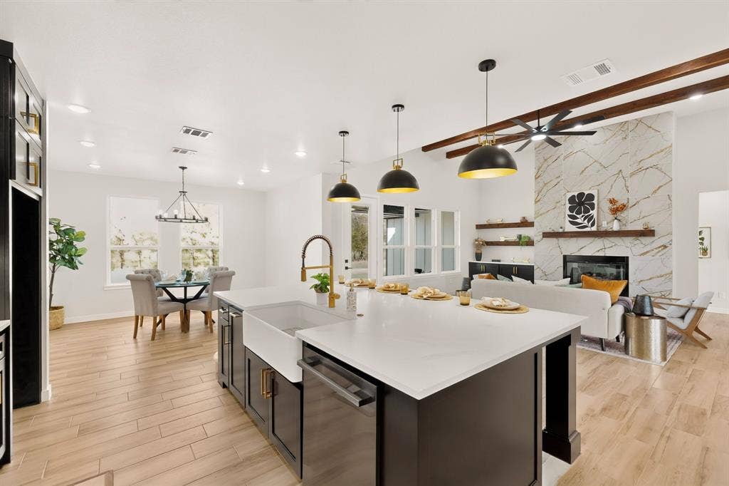 102 Nicklaus Drive, Sulphur Springs, TX 75482 Kitchen featuring a large island with a farmhouse sink and quartz countertops, wood-finish flooring, ceiling beams, and a fireplace with stone-patterned surround