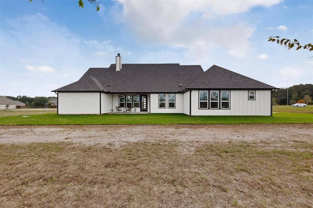 102 Nicklaus Drive, Sulphur Springs, TX 75482 Modern exterior featuring white vertical siding, a dark shingled roof, a chimney, and black-trimmed windows