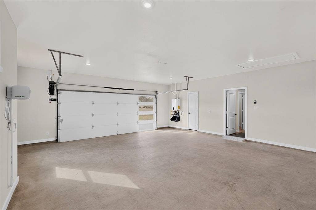 102 Nicklaus Drive, Sulphur Springs, TX 75482 Spacious multi-car garage featuring a sectional door with frosted light inserts, recessed ceiling lighting, a tankless water heater, and an attic access panel