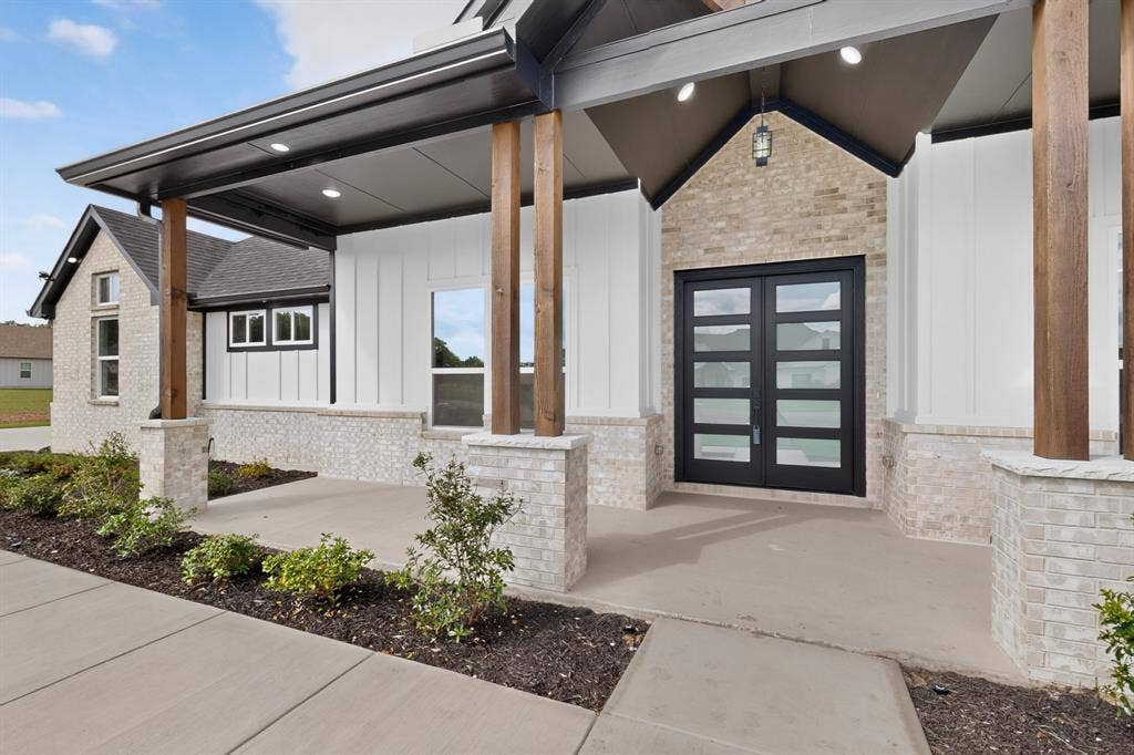 102 Nicklaus Drive, Sulphur Springs, TX 75482 Covered entry featuring a brick and vertical-panel facade, custom double doors with horizontal glass insets, exposed wood columns, and recessed lighting