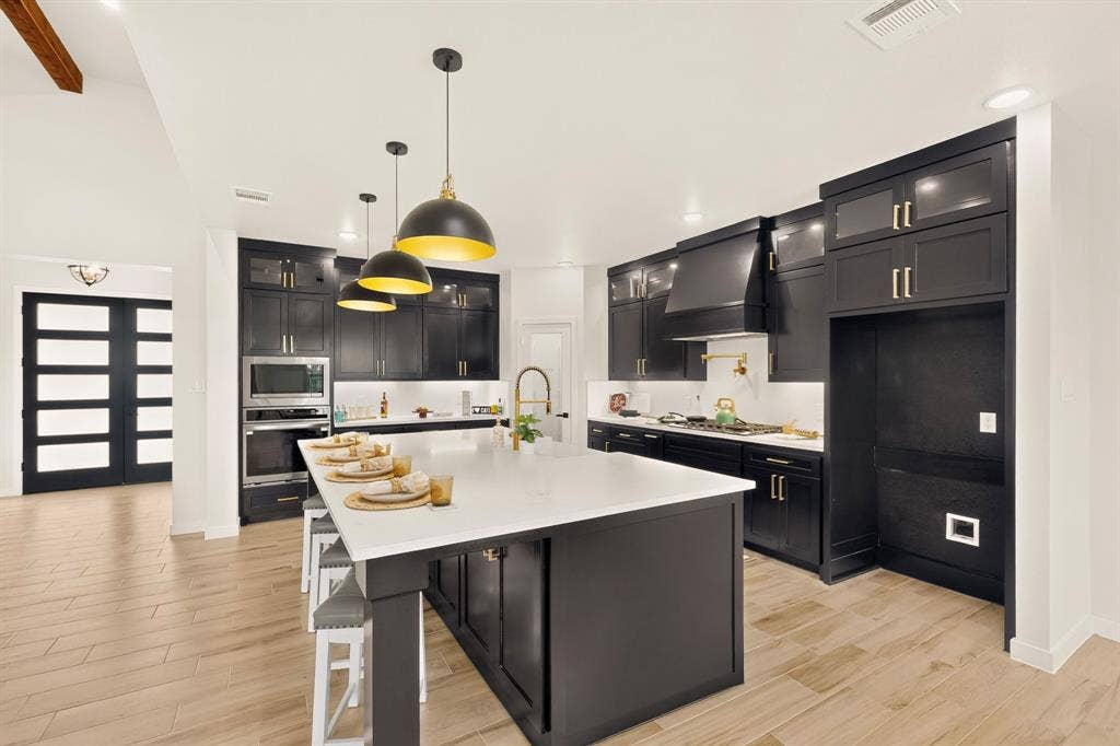 102 Nicklaus Drive, Sulphur Springs, TX 75482 Kitchen featuring black cabinetry, a large central island with a light-toned stone countertop, wood-finish flooring, gold-tone hardware, and three pendant lights