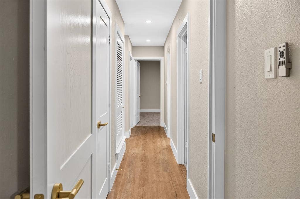 Hallway featuring wood-finish flooring, recessed lighting, white panel doors with gold-tone hardware, and a louvered closet door