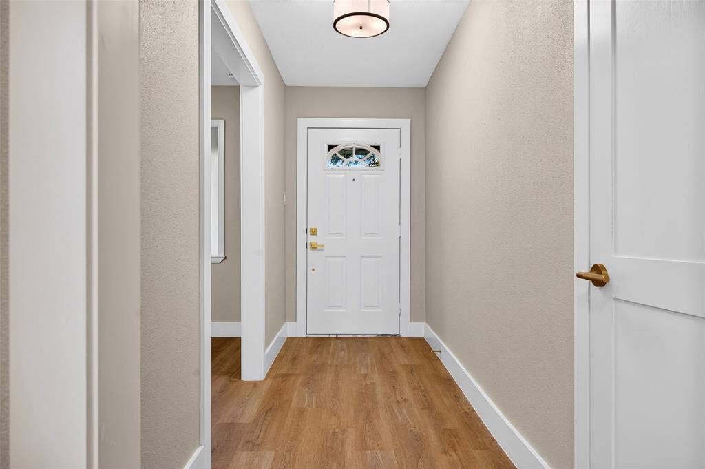 Entryway featuring wood-finish flooring, a white paneled front door with an arched glass inset, and a circular drum flush-mount light fixture