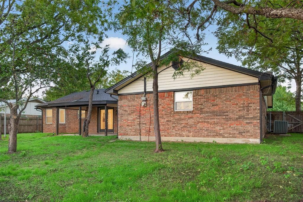 Exterior rear elevation featuring brick siding, horizontal board accents, a covered patio, and mature trees on the grounds
