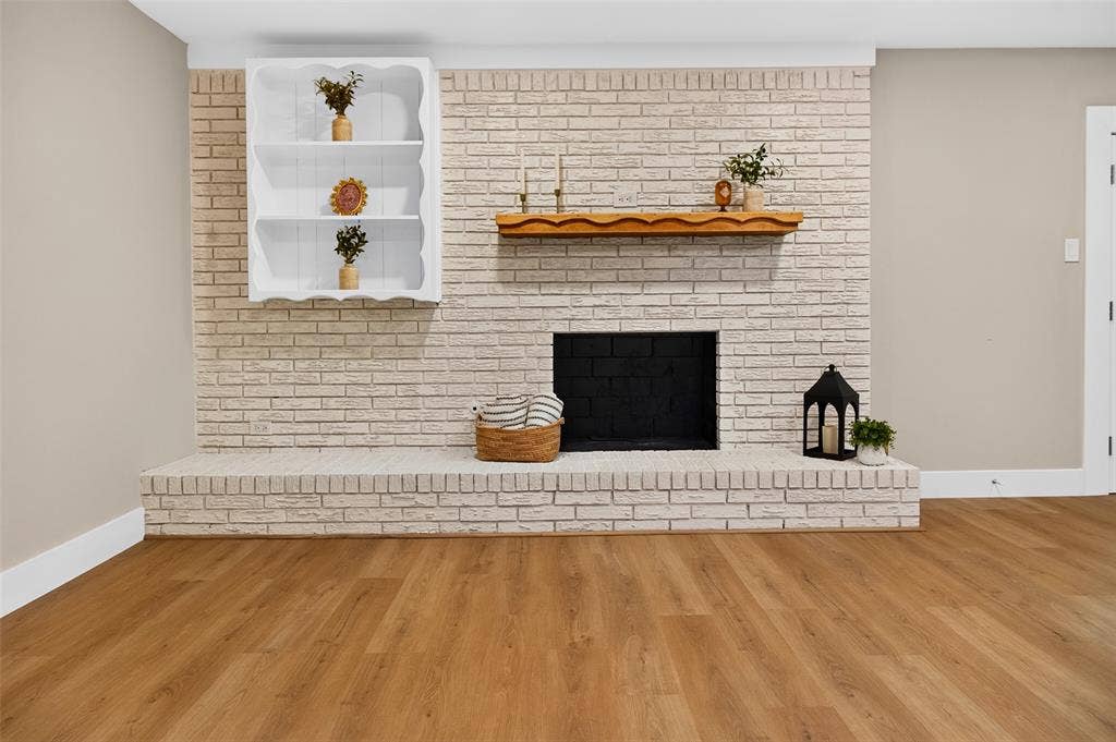 Floor-to-ceiling whitewashed brick fireplace featuring a wood mantel, raised masonry hearth, built-in recessed shelving, and wood-finish flooring
