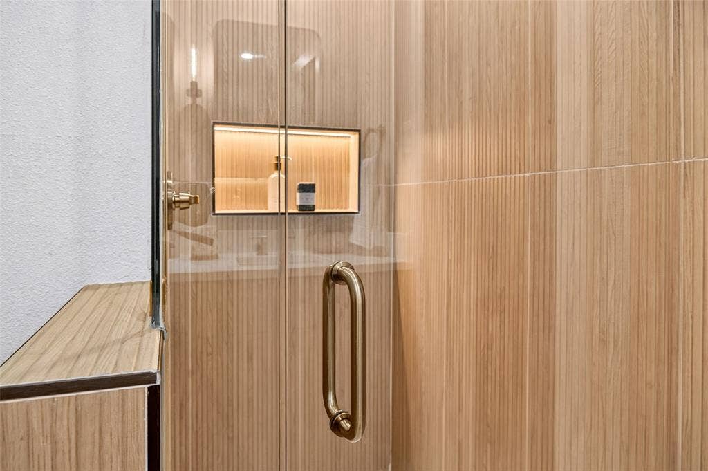 Walk-in shower featuring vertically-oriented wood-finish wall tile, a frameless glass door with a metallic finish handle, and a built-in recessed niche with integrated accent lighting