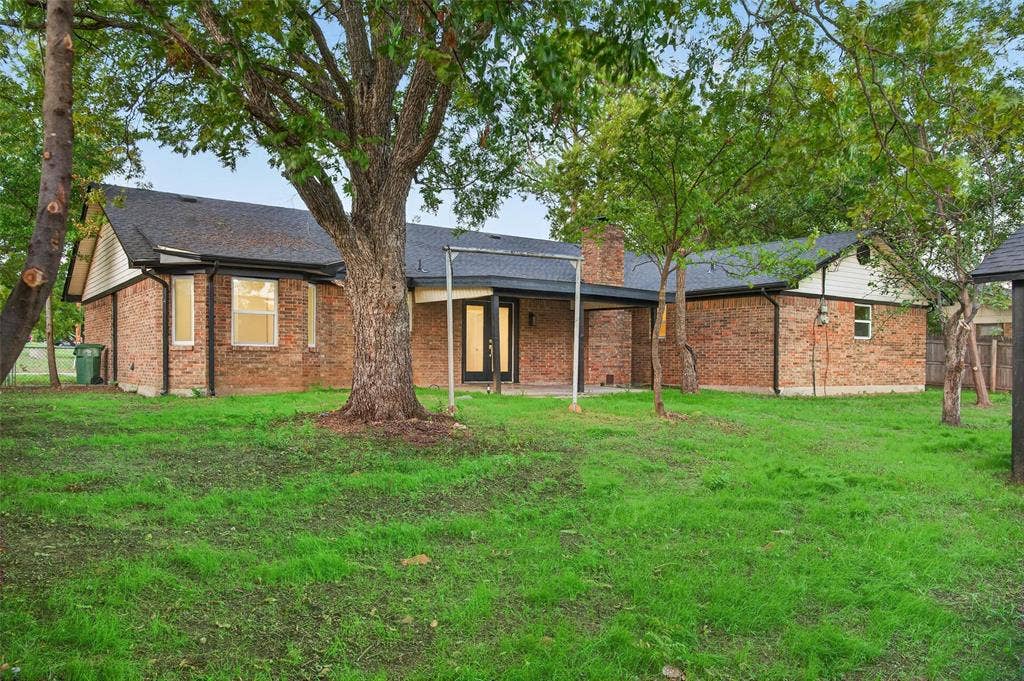 Brick exterior featuring a covered patio, brick chimney, and mature trees