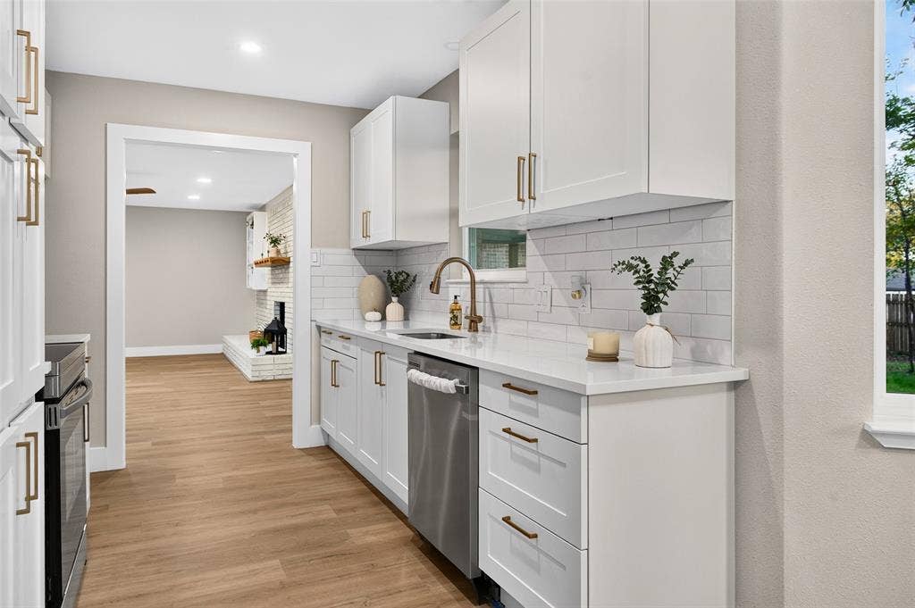 Kitchen featuring white shaker-style cabinetry, solid-surface countertops, a white subway tile backsplash, stainless steel dishwasher, and metallic hardware