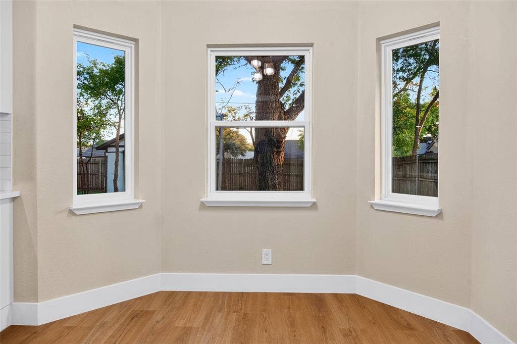 Bay area featuring three expansive windows with white trim and wood-finish flooring