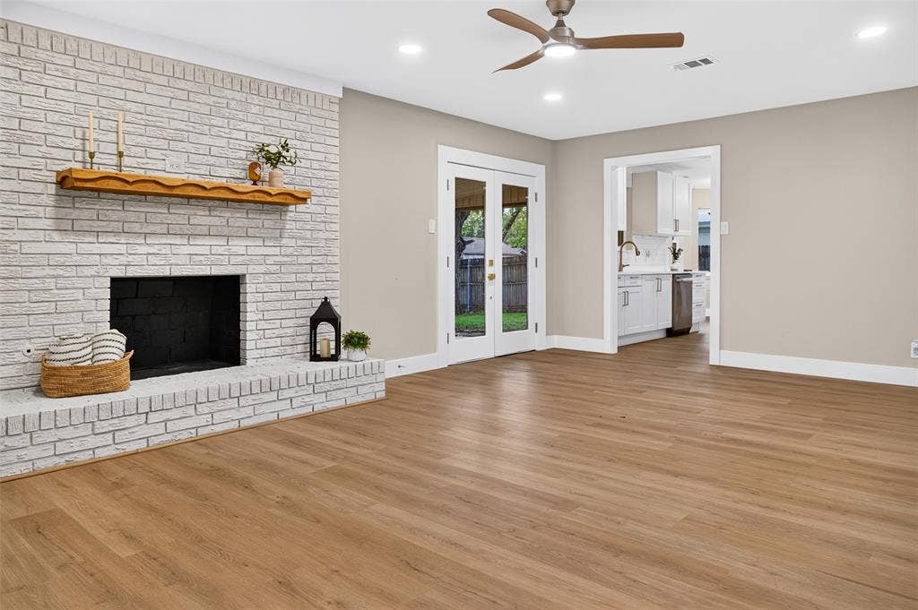 Painted brick fireplace with a wood mantel, wood-finish flooring, ceiling fan, and double-paned glass doors