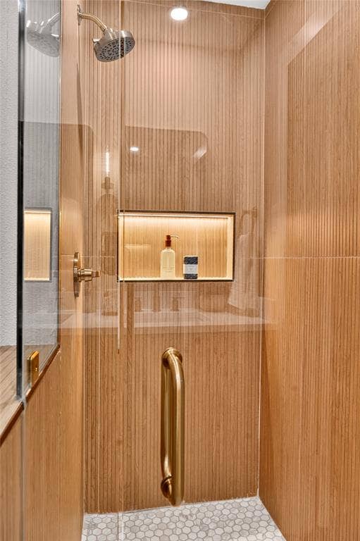 Walk-in shower featuring vertically ribbed wood-finish wall tile, frameless glass door, metallic shower fixture, integrated recessed shelving with accent lighting, and hexagonal tile flooring