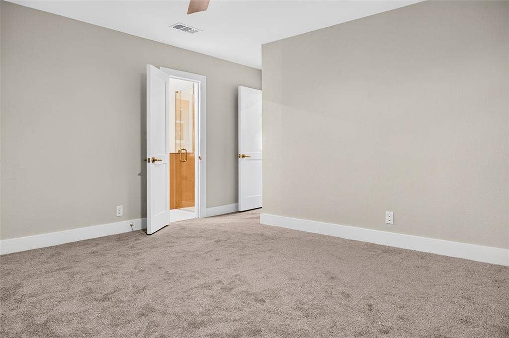 Neutral-toned interior space featuring plush wall-to-wall carpeting, crisp white interior doors with metallic hardware, and a ceiling-mounted fan