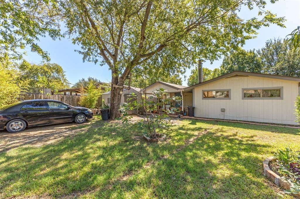 1801 Pleasant Run Road, Carrollton, TX 75006 Backyard area featuring mature trees, a dedicated gravel parking space, a detached storage structure, and brick-edged garden beds