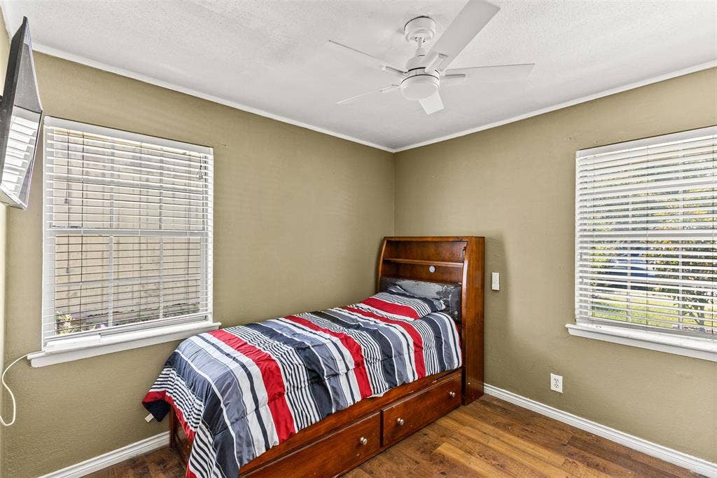 1801 Pleasant Run Road, Carrollton, TX 75006 Interior room featuring wood-finish flooring, two dual-pane windows with horizontal blinds, and a white ceiling fan with integrated lighting