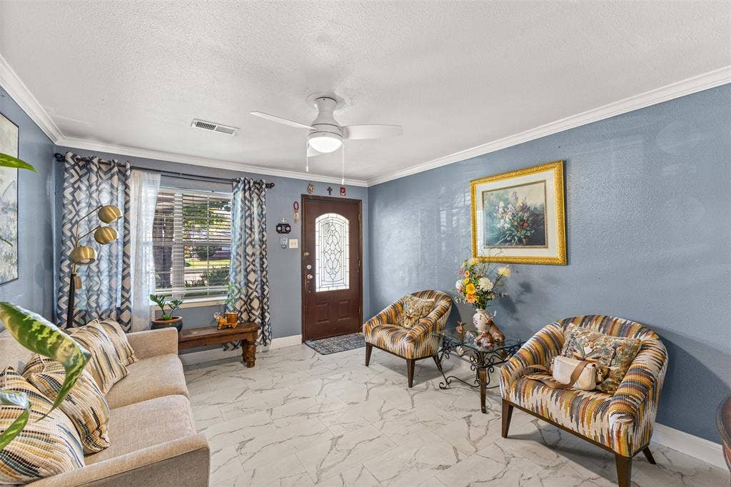 1801 Pleasant Run Road, Carrollton, TX 75006 Entryway featuring stone-finish tile flooring, a solid-core front door with an ornate glass inlay, crown molding, and a central ceiling fan with integrated lighting